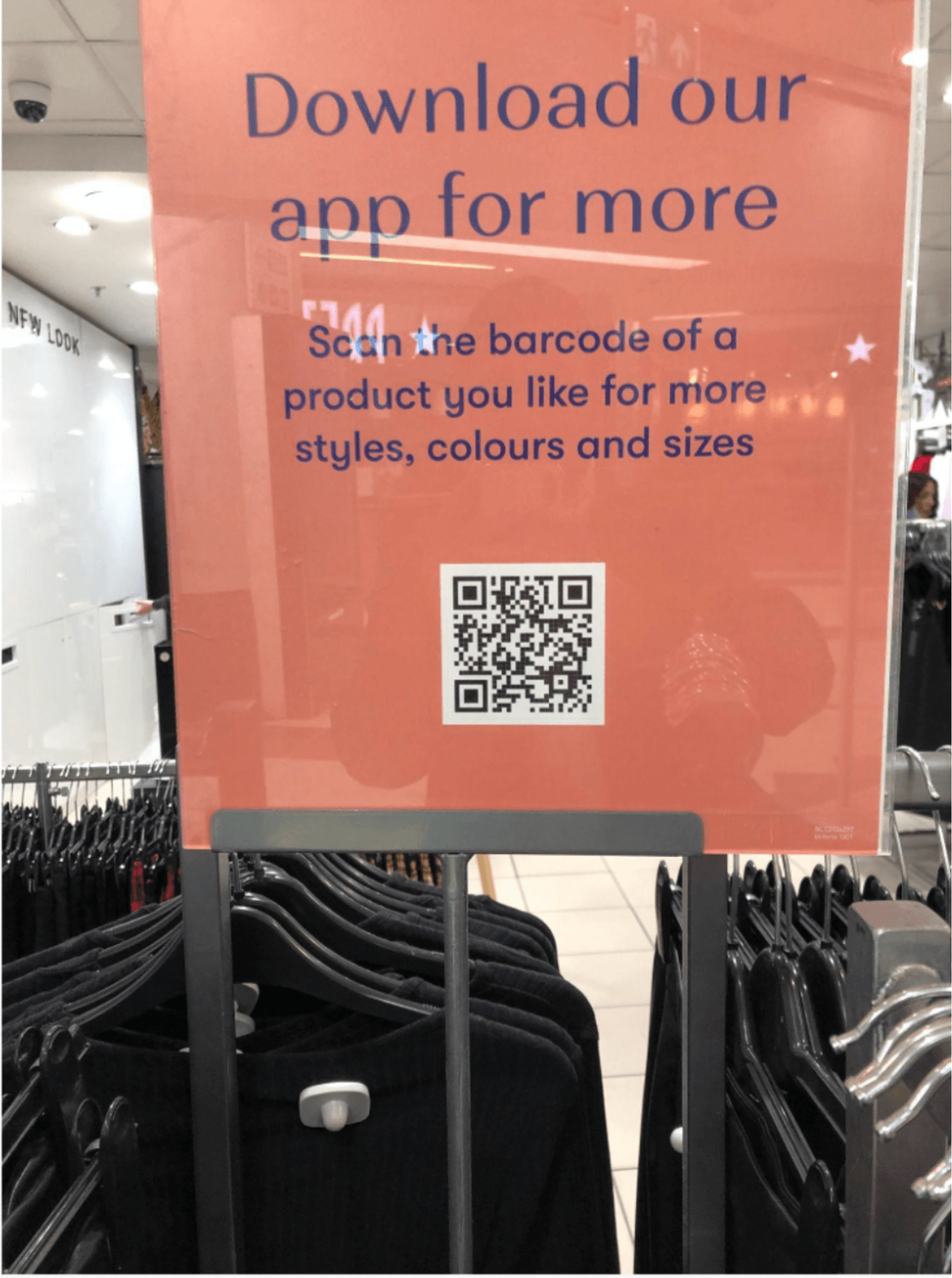 Picture of an in-store sign: "Download our app for more." The sign shows a scannable QR code to take shoppers to the app. 