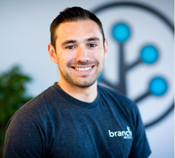 Branch Co-founder Mike Molinet smiling at camera in a Branch t-shirt in front of the Branch logo glyph